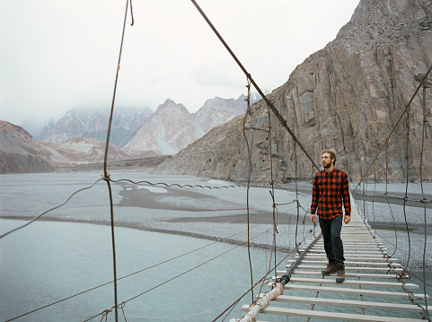 Young Caucasian man walking on suspension bridge in Pakistan