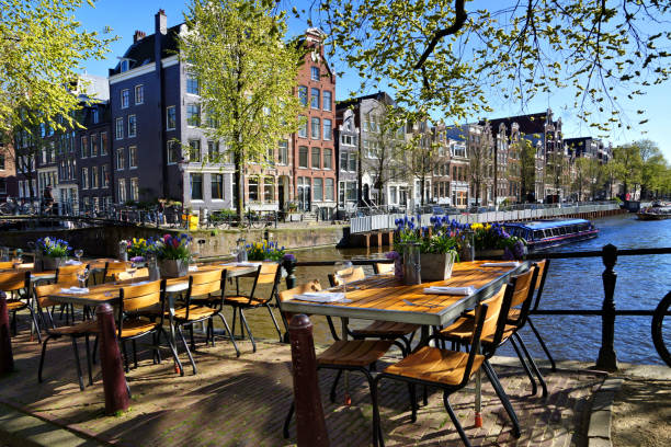 Restaurant tables lining the canals of Amsterdam during springtime, Netherlands Restaurant tables lining the beautiful canals of Amsterdam under blue skies during springtime, Netherlands benelux stock pictures, royalty-free photos & images
