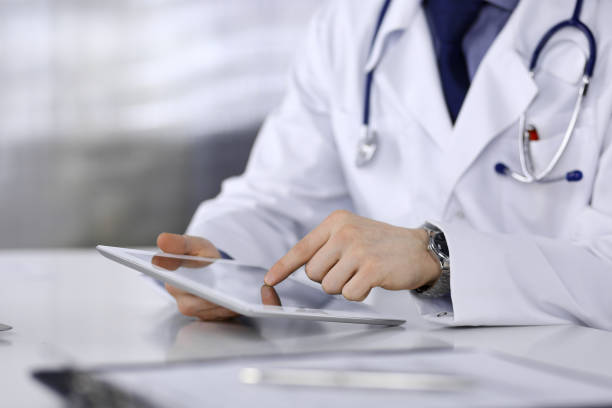 istock Unknown male doctor sitting and working with tablet computer in clinic at his working place, close-up. Young physician at work. Perfect medical service, medicine concept 1315476453