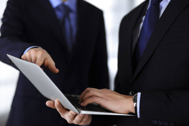istock Business people discussing a presentation at meeting, standing in a modern office. Unknown businessman with a colleague search for some information at the laptop, lawyers at negotiation. Teamwork and partnership concept 1315476459