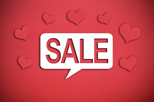 Sale written on white speech bubble, red paper hearts around, red background with copy space.