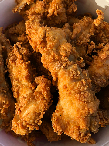 Stock photo showing fast-food takeaway of golden brown crispy, Southern fried chicken recipe, deep-fried in hot oil with seasoned spicy batter coating, herbs, flour and breadcrumbs.
