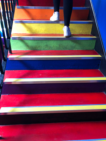 Stock photo showing close-up view looking up a modern, bright, multicoloured staircase. Rainbow effect achieved from painting steps red, blue, green, yellow and orange.