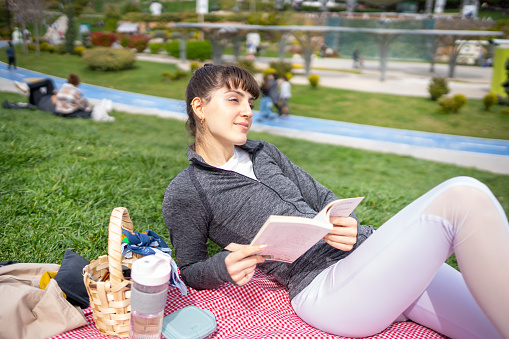 Young woman having a picnic in public park and reading book