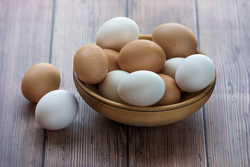 Wooden bowl with brown and white chicken eggs on wood table. Brown and white eggs in bowl on wood background. Free-range organic eggs. Healthy food concept
