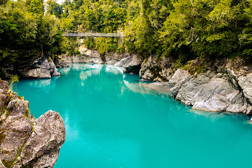 In this April 2021 image taken on a cloudy day, the turquoise waters of the Hokitika River flow under a swing bridge at this popular tourist destination near Hokitika, Aotearoa New Zealand.