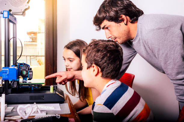 Happy children learning to 3D print with a young adult stock photo