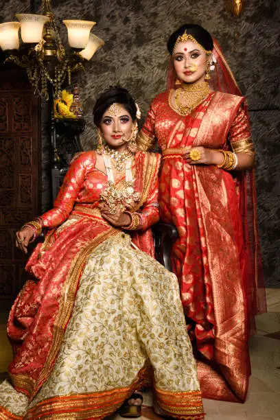 Photo of Magnificent young Indian brides in luxurious bridal costume with makeup and heavy jewellery with classic vintage interior in studio lighting. Wedding Lifestyle and Fashion