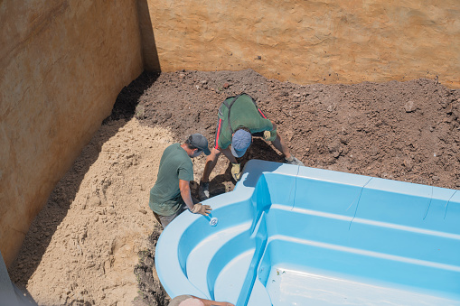 Construction workers are installing a swimming pool at a house backyard