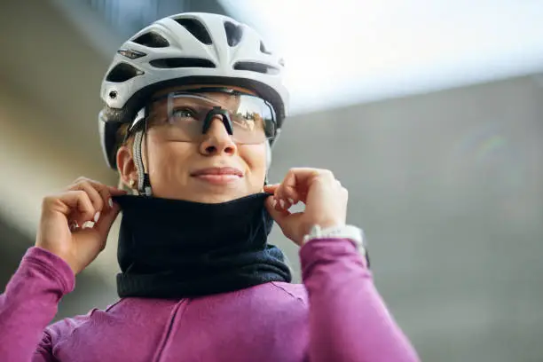 Portrait of professional female cyclist wearing pink suit and neck warmer smiling away while getting ready for training, standing outdoors on a daytime. Sport, biking, people concept