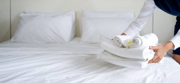 ベッドに白い花を持つタオルのセットを置くホテルのメイド。ホテルのゲストのための部屋を準備する青い制服を着たスタッフ。 - bedroom hotel hotel room inn ストックフォトと画像