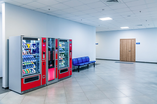 Group of red vending machines stands by the wall inside public building. No people. Unmanned store. Copy space for your text. Small business theme.