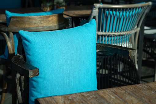 A bright blue color backrest pillow on cozy style chair and table set without people. Interior decoration object, close-up photo.