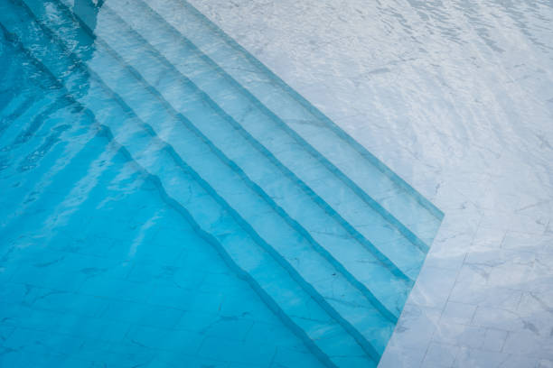 Swimming pool with transparent blue water and white marble luxury floor. Beautiful designed swimming pool with transparent blue water and white marble luxury floor. Sport recreation and background photo. standing water photos stock pictures, royalty-free photos & images