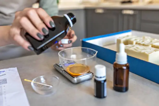 A soap-maker woman weighs aromatic oils for making cosmetics on a kitchen scale. Home spa. Small business.