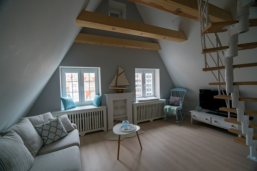 Interior of cozy attic apartment in scandinavian style, with wooden furniture and rocking chair.
