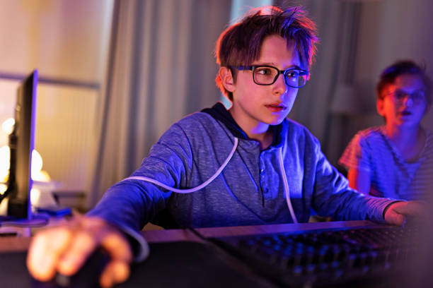 мальчики-подростки играют в многопользовательские онлайн игры с помощью настольного пк - teenager video game gamer child стоковые фото и изображения