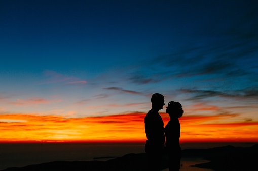 Silhouettes of a couple holding hands against the background of the sunset in the mountains. Close up. High quality photo