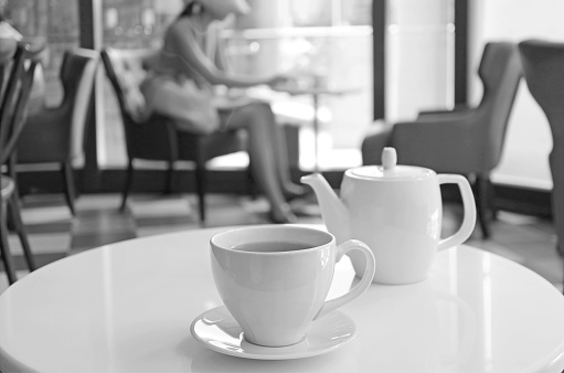 Monochrome porcelain teacup and pot on a round table in a cafe, ( Self Portrait )