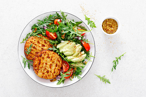 Grilled chicken burgers, avocado and fresh vegetable salad with tomato and arugula