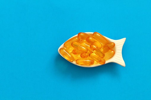dietary supplement omega in a white bowl in the shape of a fish, vitamins in a bowl like a fish in the sea, fish oil capsules on a blue background, healthy lifestyle concept