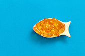 omega vitamin in transparent yellow capsules in a white bowl in the shape of a fish on a blue background