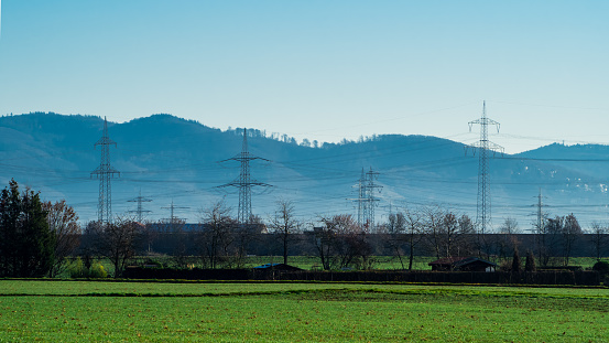 Landscape with green agricultural field, trees, power lines, hills, blue sky in background