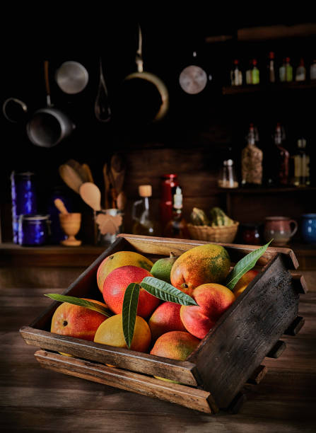 Tropical fruits in rustic kitchen: Wooden crate with assorted mangos. Natural lighting