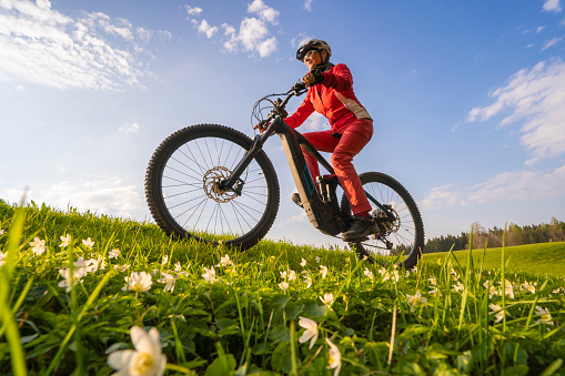 pretty mid age woman riding her electric mountain bike in early springtime in the Allgau mountains near Oberstaufen, in warm  light with blooming spring flowers in the Foreground