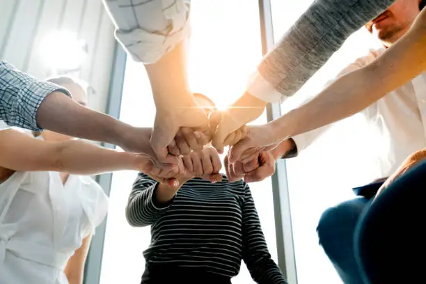 Photo of Close up top view of young and freshness energy business people putting their strong hands together. Stack of friendship hands. Unity and successful teamwork concept.
