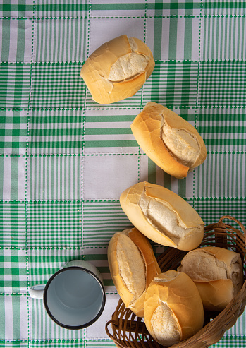 breads in a basket and mug on checkered tablecloth over rustic wood, black background, top view.