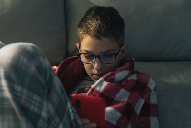 istock Child in dressing gown on sofa using mobile phone 1315631170