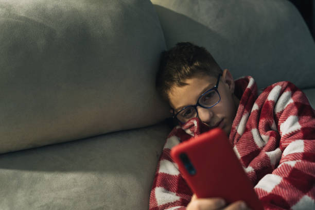 istock Child in dressing gown on sofa using mobile phone 1315631776