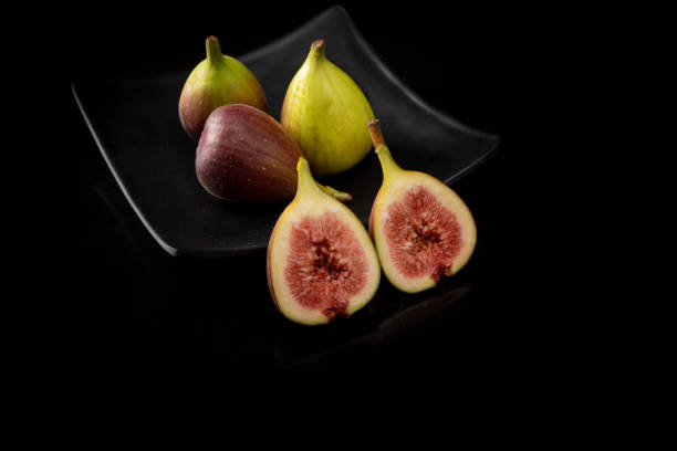 istock Purple figs, purple figs open on a black plate on dark reflective surface, black background, selective focus. 1315634001