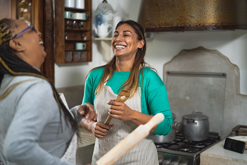 Happy multiracial women having fun in the kitchen preparing a homemade recipe in vintage house