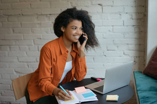 istock Confident businesswoman using laptop, talking on mobile phone, taking notes working in office 1315651050