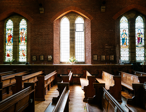 Color image depicting the interior architecture of an Anglican church in Crawley, UK. The church is fitted with oak pews and has majestic stained glass windows.