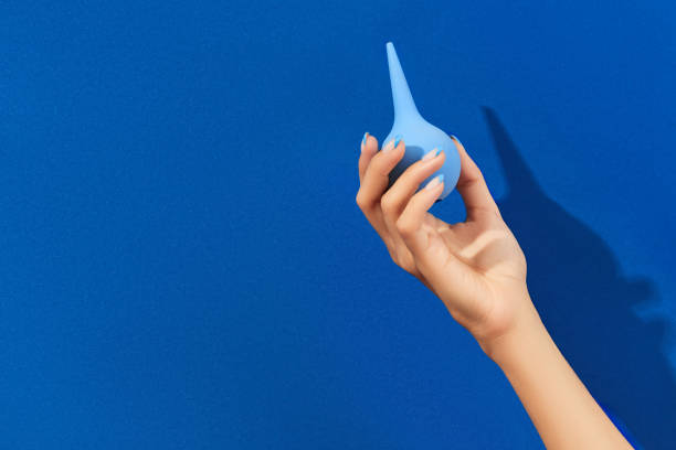 istock Wellgroomed womans hand holding enema on blue background 1315651943