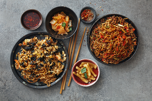 Spicy Korean beef noodles (Shin Ramyun). Noodle with seafood such as shrimp, squid, baby octopus and crab are braised in spicy seasoning with various vegetables (Haemul Jjim). Flat lay top-down composition on concrete background.