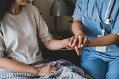 Close-up of a female nurse holding hands for reassuring her female patient on bed.