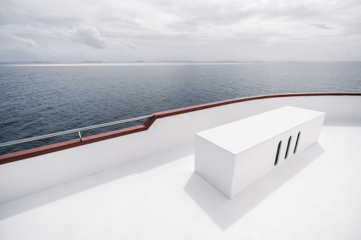 A wide-angle view from the upper deck of a safari yacht with a rectangular box bench with three holes from the ventilation system, lit by the hot summer sun, with a seascape in a defocused background