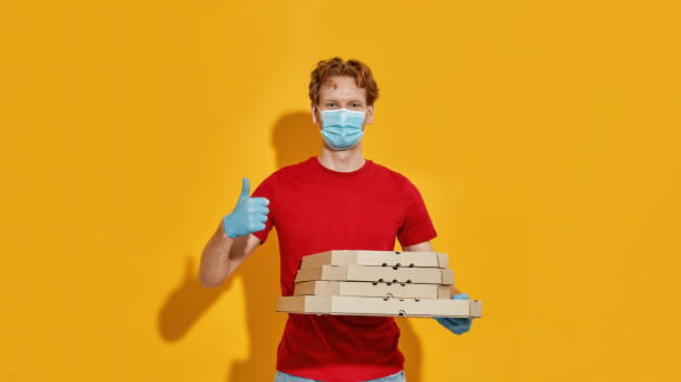 istock Young caucasian courier in mask holding pizza boxes t 1315673109