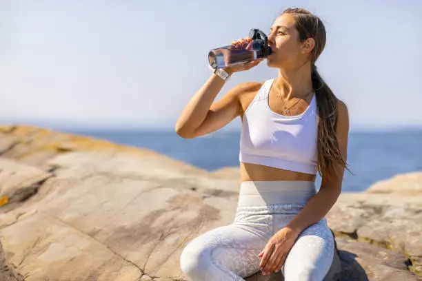 Photo of Female Athlete Drinking Water During Outdoor Workout by the Sea