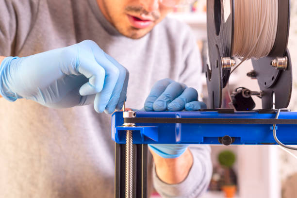 primer plano de la mano de un hombre con guantes azules calibrando una impresora 3d. - 3d printing fotografías e imágenes de stock