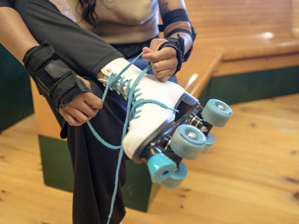 Close up og Young black woman rollerskating indoors. She is tiding up her shoelaces  on old fashion roller skates. Dressed in casual summer outfit with hand and elbow pads for protection. Interior of bowling alley and restobar closed for regular business.