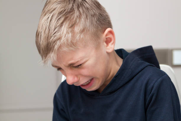 sad hurt little boy is crying with his head down stock photo
