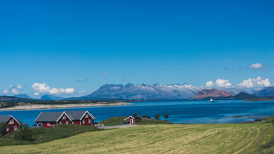 Traditional norwegian houses at a beautiful fjord with blue, clear water and snowy mountains in the background. Sunny weather