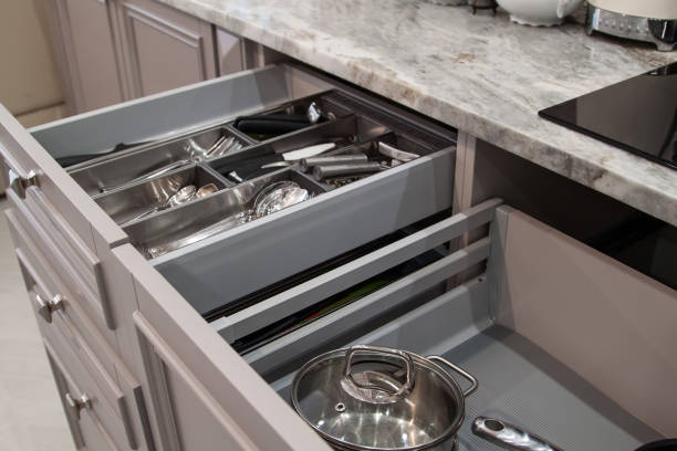 istock Opened drawers with cutlery, utensils, pots and pans inside in beige kitchen with marble countertop 1315720901