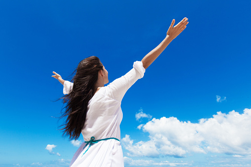 Young woman with raised hands and cloudy sky background