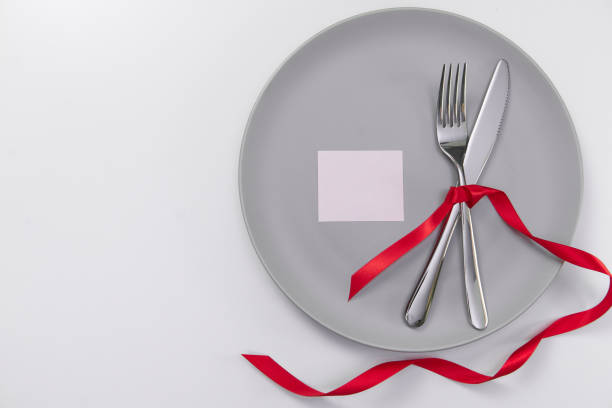 istock Festive table setting with red ribbon. Fork and knife on a gray plate and card postcard for text. Copy space. 1315735618